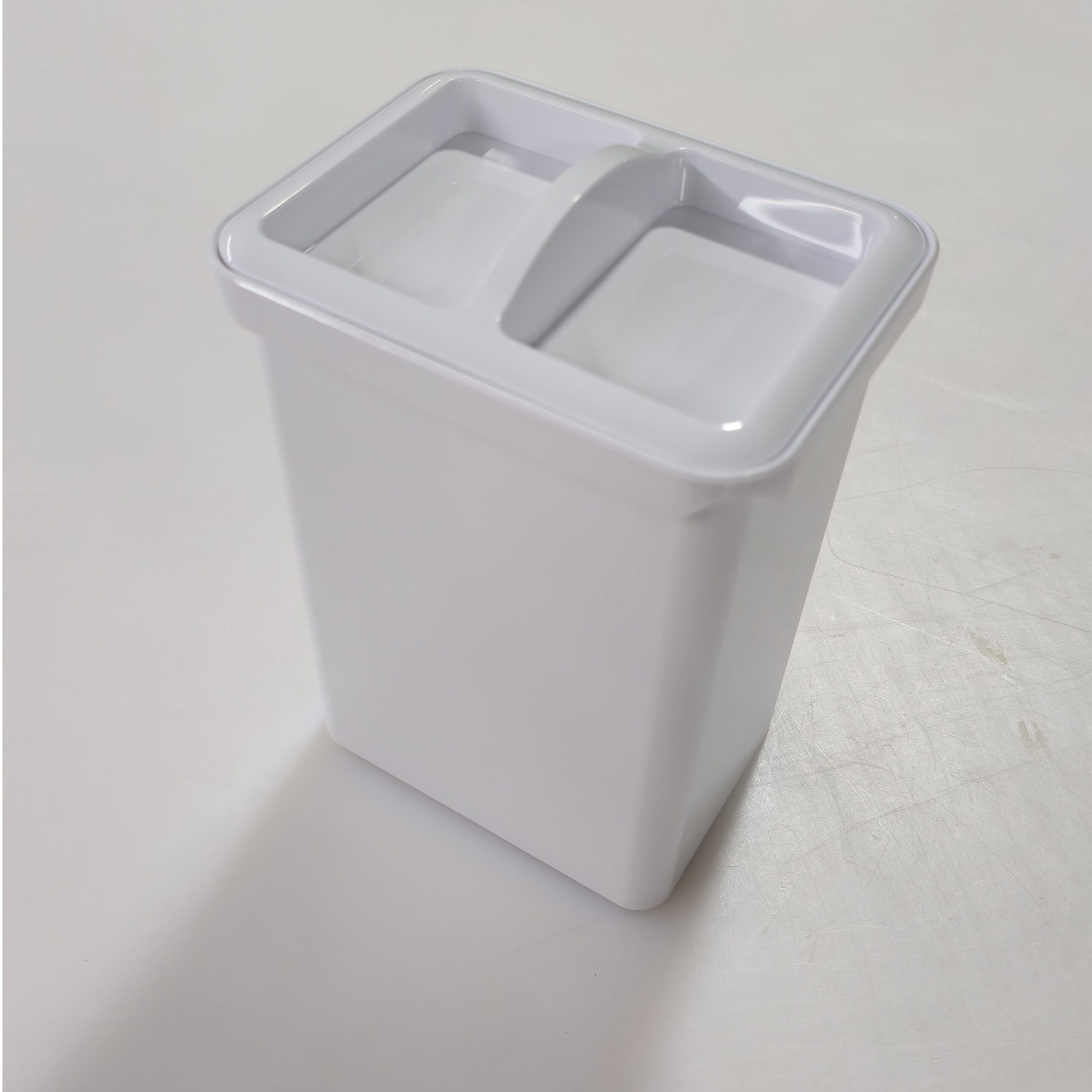 A white rectangular plastic container with a divided lid sits on a plain, light-colored surface.